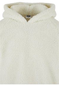 Sweat à capuche sherpa duveteux couleur crème avec une capuche et une étiquette visible à l'intérieur du col portant la mention Urban Classics.