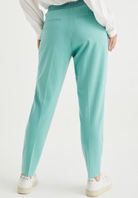 Ljus teal taperedbyxor med en slät yta, elastisk midja och två bakfickor. Matchas med vita sneakers.