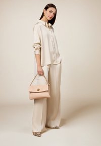 Cremefarbene Satinbluse mit Knopfdetails, kombiniert mit weit geschnittenen Hosen. Hält eine hellrosa Lederhandtasche mit einem goldenen Verschluss und Kettenhenkel.