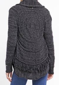 Dunkelgrauer Cardigan aus Strickstoff, mit einem strukturierten Spiraldesign auf der Rückseite und angedeuteten Fransen am Saum. Lange Ärmel sind enthalten.