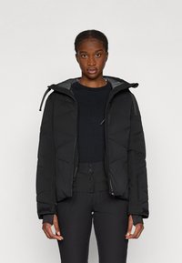 Melnas gumijas pufīgas jakas ar pelēku kapuci, ar rāvējslēdzēju priekšā, regulējamiem stingiem un elastīgām piedurknēm.