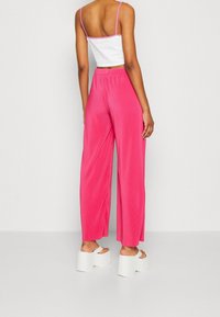 Rosa vida byxor med struktur, med ett elastiskt midjeband och sprund i bensluten, tillsammans med vita blockklack sandaler.