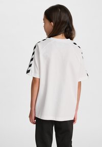 T-shirt en coton blanc avec des motifs rayés noirs sur les épaules. Manches courtes et coupe décontractée. Design simple avec encolure ras du cou.