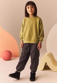 Pullover verde con tessuto texturizzato e spalle scese, abbinato a pantaloni cargo grigi scuri a vestibilità ampia e stivaletti neri alla caviglia.