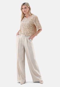 Beiger Paillettenoberteil mit kurzen Ärmeln, kombiniert mit hellen, weit geschnittenen Hosen. Glatte Textur und dezenter Glanz durchgehend.