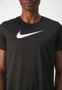 Camiseta de manga corta negra hecha de un tejido ligero, con un destacado logotipo en blanco de Nike en el pecho. Textura suave.