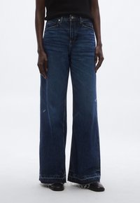 Sötét árnyalatú, bő szárú farmernadrág rojtos szegéllyel, első zsebekkel és enyhe kopottsággal. Pamutból készült, sima tapintású anyagból.