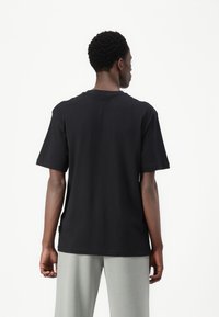 Sort bomulds T-shirt med korte ærmer og rund halsudskæring, synlig syning og en afslappet pasform, vist fra ryggen.