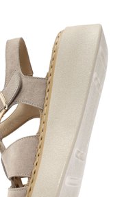 Sandalo alla caviglia color beige chiaro con tomaia in suede testurizzato. Presenta una spessa suola piatta bianca con una leggera curva e cuciture decorative.