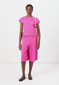 Κοντό ροζ μπλουζάκι με μανίκια καπάκι, συνδυασμένο με κοντές σορτς στο γόνατο. Το μοντέλο φορά μαύρα φλατ παπούτσια και κρατά μια ανοιχτόχρωμη τσάντα ώμου.