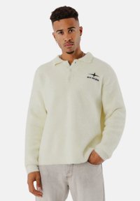 Weißer Fleece-Pullover mit einem Kragen, ausgestattet mit einem schwarzen gestickten Logo auf der linken Brust und langen Ärmeln. Strukturierter, weicher Stoff.