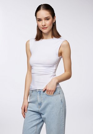 Top bianco senza maniche con un design aderente, abbinato a jeans blu chiaro con decorazioni. Tessuto morbido e dettagli minimali.