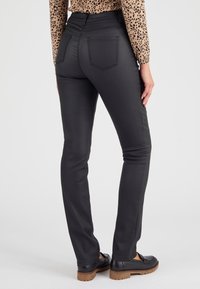 Pantalones negros ajustados con una textura suave, que cuentan con dos bolsillos traseros y un diseño de cintura alta. Combinados con zapatos negros y una blusa de lunares.