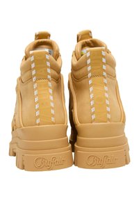 Par av sandfärgade platåsneakers med tjocka sulor, märkta med "Buffalo" präglat på hälarna och vertikala dragflikar med vit randig detalj.