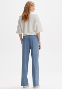 Haut blanc à côtes et pantalon large bleu clair avec une taille élastique. Modèle de dos, montrant des détails au dos et des lignes épurées.