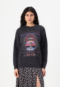 Felpa nera con stampa grafica che presenta montagne, un pianeta e il testo "BILLABONG WORLD TOUR 1973." Oversize, tessuto morbido, colletto a girocollo.