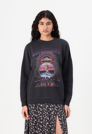 Sweatshirt noir avec impression graphique représentant des montagnes, une planète et le texte "BILLABONG WORLD TOUR 1973." Coupe oversized, tissu doux, col rond.