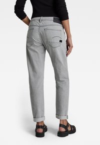 Pantalon en denim gris, conçu avec une coupe décontractée, présentant des ourlets roulés, deux poches arrière et un empiècement en cuir noir avec logo à la taille.