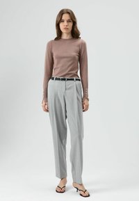 Lichtbruine top met lange mouwen en knoopdetails bij de polsen, gecombineerd met lichtgrijze, hooggetailleerde broek en zwarte riem, met een losse pasvorm.