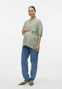Blusa premaman in verde menta con pois neri, design avvolgente, maniche corte; abbinata a jeans blu larghi e ballerine a punta.
