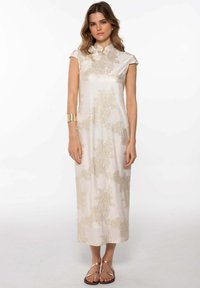 Robe midi blanche avec un motif texturé subtil en or. Dispose d'un col haut et de manches courtes. Accompagnée d'accessoires en or.