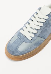 Sinine samet ja nahk sneaker, valgete nööride ja kummitald ikk. Üksikasjad on tikitud ning materjal on pehme.