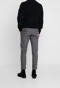 Svart stickad tröja i kombination med grå rutiga byxor. Byxorna har smal passform och två bakfickor med knappar. Skorna är svarta i mocka.