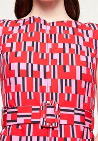 Colorful dress featuring a geometric pattern in red, pink, and black, with a fitted belt and square buckle, made of smooth fabric.