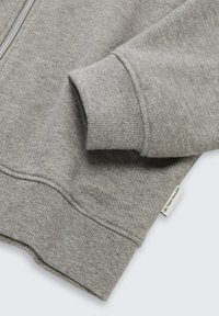 Felpa grigia con zip, maniche a costine, una texture morbida e un piccolo etichetta del marchio sull'orlo. Il tessuto presenta un leggero effetto lucido.