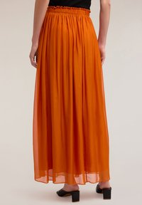 Gonna maxi arancione con tessuto fluido e trasparente e vita elasticizzata, caratterizzata da una consistenza liscia e un design lungo fino alla caviglia. Sandali neri con tacco a blocco.