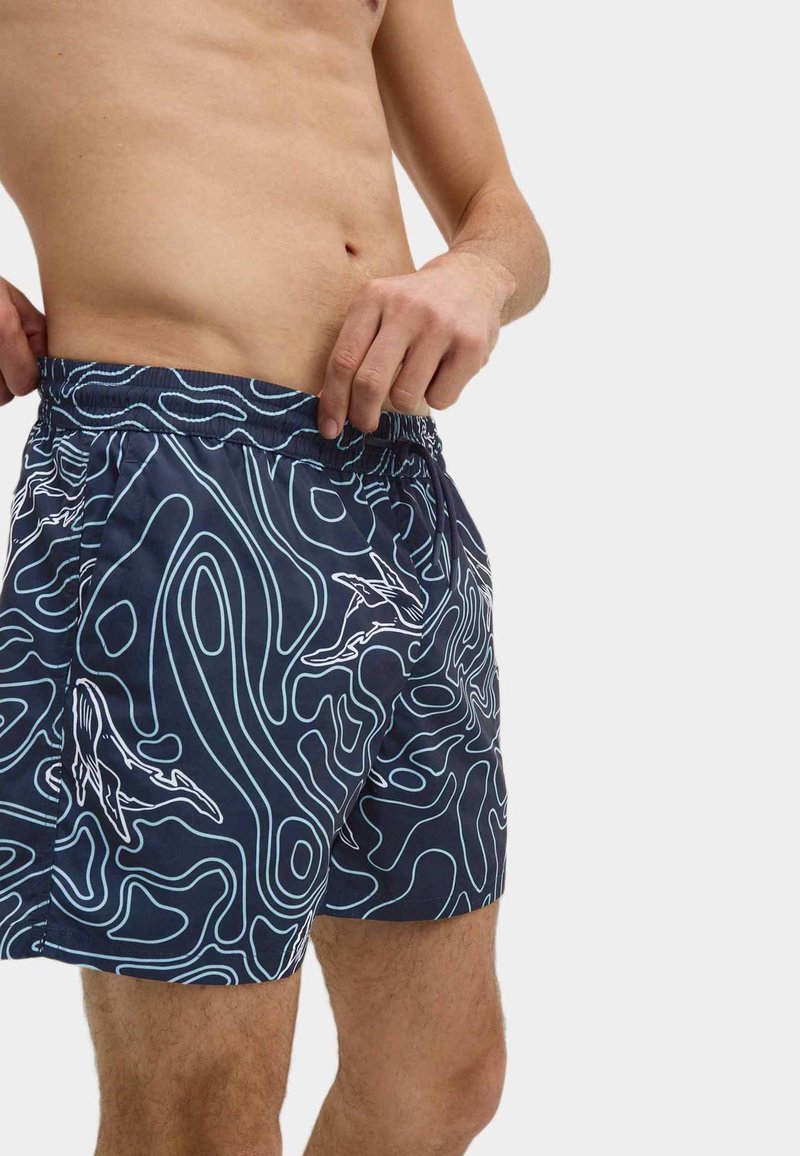 Zwemshorts in donker marineblauw met een golvend patroon in wit. Elastische tailleband met een trekkoord. Boven de knie lengte, lichtgewicht stof.