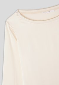 Maglietta a maniche lunghe in tessuto crema chiaro con scollo rotondo, caratterizzata da una sottile trama a righe e un bordo a contrasto lungo il colletto.