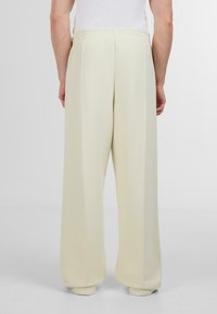 Pantaloni largi, bej deschis, realizati dintr-un material neted si moale. Au un talie elastica si cusaturi drepte pe laterale.