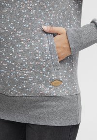 Sudadera gris con patrones circulares en azul claro y rosa, que cuenta con un bolsillo canguro, puños acanalados y un logotipo de marca de cuero.
