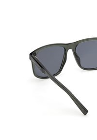 Czarne okulary przeciwsłoneczne z ciemnymi soczewkami, posiadające elegancką plastikową oprawę i wąskie zauszniki. Projekt jest kanciasty i minimalistyczny.