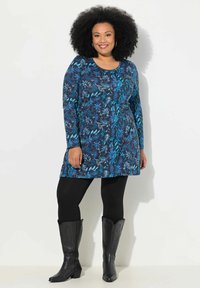 Langsleeve jurk in donkergroen met bloemmotieven in turquoise. Draagt over zwarte leggings en gecombineerd met zwarte cowboylaarzen.