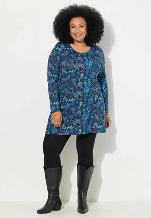 Langærmet kjole i mørkeblå med blomsterprint i turkis. Båret over sorte leggings og kombineret med sorte cowboystøvler.