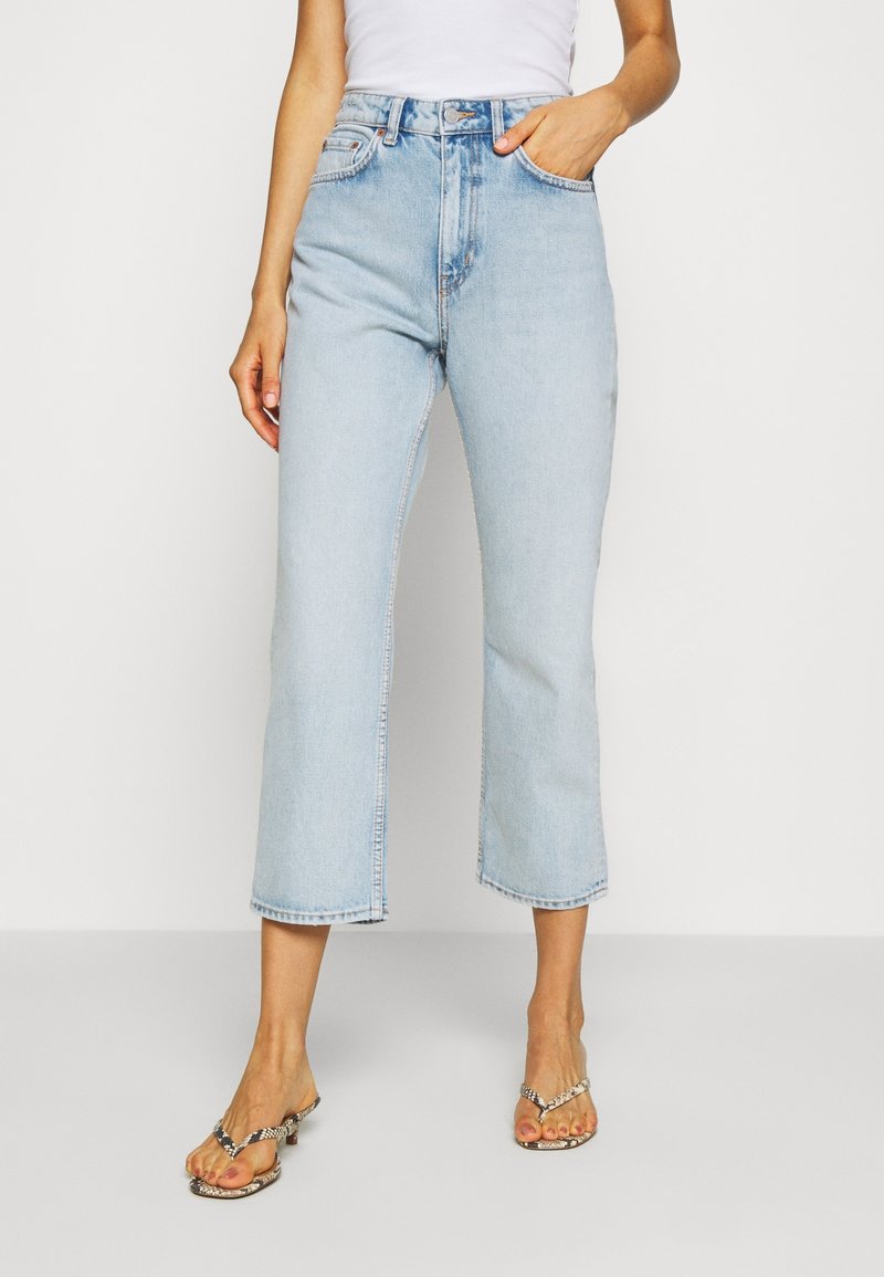 Jean denim bleu clair court avec taille haute, jambe légèrement évasée et légère décoloration. Fini avec un design classique à cinq poches et passants pour ceinture.