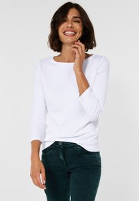 Witte, lange mouwen shirt met een ronde hals, gemaakt van zachte stof, gecombineerd met donkergroene jeans met een slim fit en gebogen zoom.
