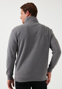 Pullover grigio in pile con colletto alto, maniche lunghe, polsini a coste e orlo dritto. Tessuto liscio, dettagli minimi e senza loghi visibili.