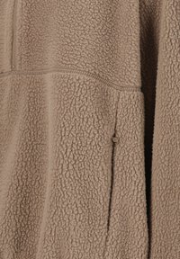 Brauner Fleece-Pullover mit weicher, texturierter Oberfläche, ausgestattet mit einem Viertel-Reißverschluss und einer Seitentasche mit einem kleinen Zugband.