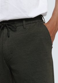 Dark green elastic waist pants with a textured fabric, featuring a drawstring closure and side pockets, paired with a white shirt.