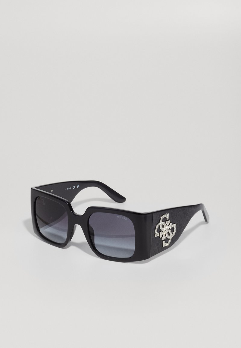 Gafas de sol negras de gran tamaño con lentes degradados. El acento del logo de strass transparente en el lateral añade detalle, mientras que la montura mate presenta un acabado texturizado.