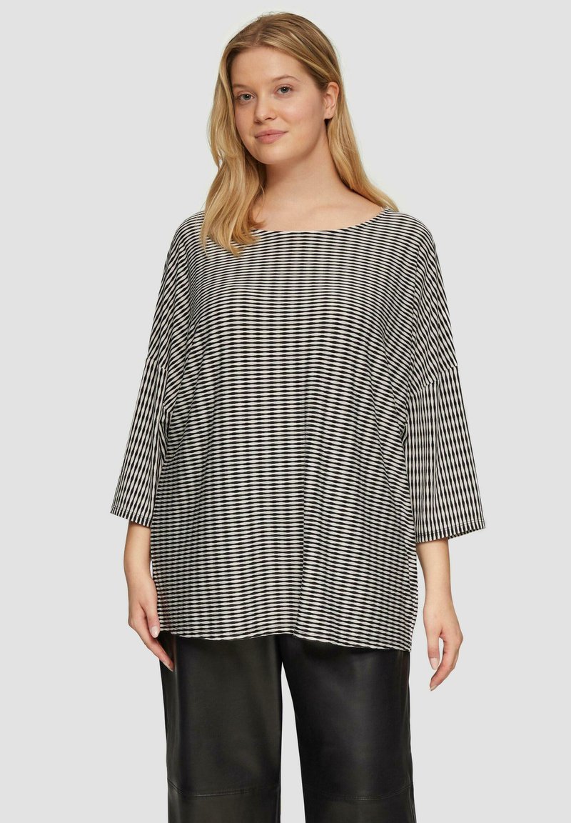 Zwart-wit gestreepte oversized top met een wijde halslijn en driekwartmouwen, gecombineerd met zwarte leren broek.