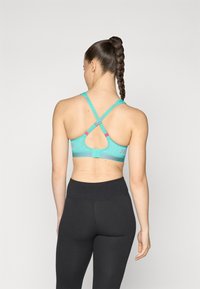 Turkisesport BH med meshrygg, krysstrapped, og justerbart bånd; har dekorative detaljer i rosa og grå.