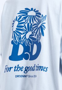 Helles blaues Baumwoll-T-Shirt mit auffälligem blauen Blumen-Design, großen "DD"-Buchstaben und dem Text "Für die guten Zeiten."