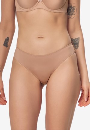 Kobieta w cielistym, bezszwowym bieliźnie i biustonoszu, z tatuażami kota i ryczącego wielkiego kota na ramionach.