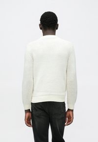 Beli pleteni pulover z dolgimi rokavi, rebrastimi manšetami in spodnjim robom. Teksturiran vzorec, okrogel izrez. Kombiniran s temno modrimi kavbojkami.