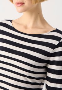 Randig topp med horisontella marinblå och vita ränder, rund halsringning och mjuk tygtextur, sedd från axeln till nacken.
