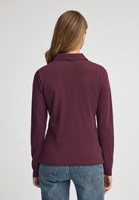 Burgundy långärmad polo skjorta med krage, tillverkad av slät tyg, med en figurnära design och sidofickor vid fållen.
